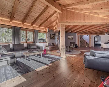 Geräumiger offener Wohnbereich mit Holzbalkendecke, großen Fenstern und gemütlicher Einrichtung.