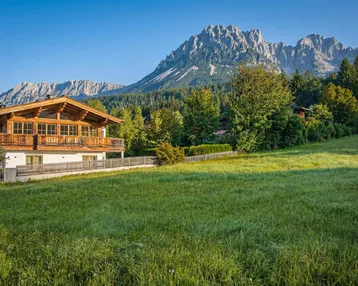 Traditionelles Chalet mit Holzbalkonen und weitem Blick auf die Berge und grüne Wiesen.