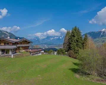 Traditionelles Holzhaus in alpiner Landschaft mit weitem Blick auf die Berge und grüne Wiesen.