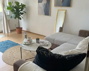 Helles Wohnzimmer mit modernem Sofa, Couchtisch und dekorativen Bildern an der Wand.