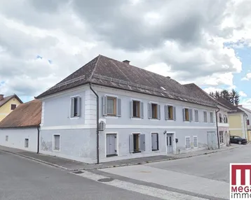 Historisches Gebäude mit hellblauer Fassade, grauen Fensterläden und Satteldach in ländlicher Umgebung.