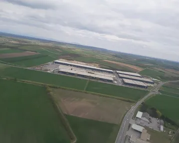 Luftaufnahme einer Industrieanlage umgeben von weiten Feldern unter bewölktem Himmel.