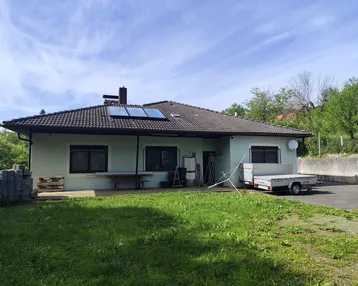 Einfamilienhaus mit Garten, Solarpaneelen auf dem Dach und einem Anhänger auf dem Vorplatz.