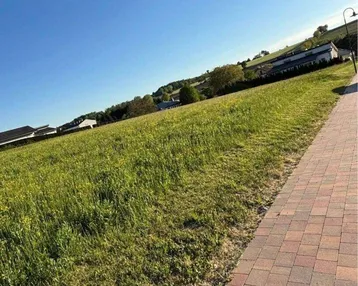 Weitläufige Grünfläche mit gepflastertem Weg und Blick auf die umliegende Landschaft unter blauem Himmel.