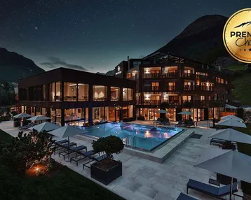 Luxuriöses Hotelgebäude mit beleuchtetem Außenpool und Liegebereich unter sternenklarem Nachthimmel.