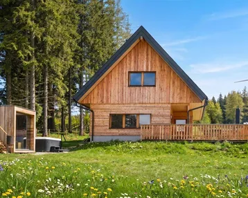 Charmantes Holzhaus mit grüner Wiese, Hot Tub und Sauna vor einem Waldhintergrund.