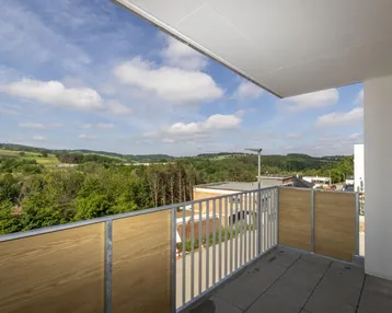 Geräumiger Balkon mit Fliesenboden und weitem Blick über die grüne Landschaft.
