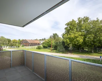 Balkon mit Fliesenboden und Blick ins Grüne, umgeben von Bäumen und ländlicher Umgebung.
