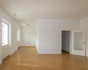 Helles, leeres Wohnzimmer mit Parkettboden und mehreren Fenstern, bereit zur individuellen Gestaltung.