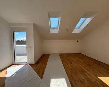 Heller Raum im Dachgeschoss mit Holzboden, Dachfenstern und Zugang zu einer Terrasse.