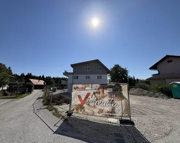 Neubau im Bau mit Werbebanner auf sonnigem Grundstück und blauer Himmel.