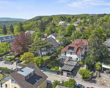 Luftaufnahme einer grünen Wohngegend mit vielen Häusern und Bäumen unter blauem Himmel.