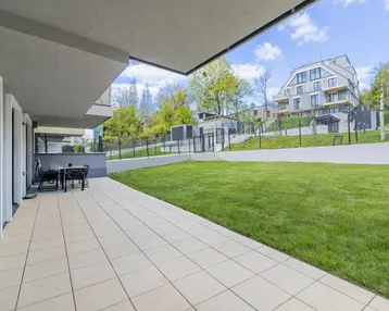 Großzügige Terrasse mit Fliesenboden und Gartenmöbeln, angrenzend an eine gepflegte Rasenfläche.