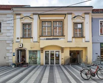 Historisches Gebäude mit Ladenlokalen im Erdgeschoss und Wohnungen darüber an einer Straße.
