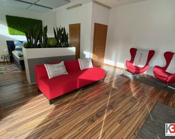 Moderner Empfangsbereich mit rotem Sofa, bequemen Sesseln und Holzboden, der zum Verweilen einlädt.