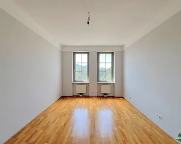 Helles Zimmer mit Parkettboden und zwei Fenstern, bereit zur individuellen Gestaltung.