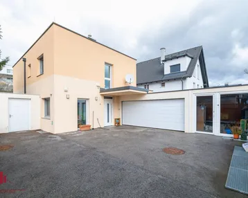 Moderne Hausfassade in Beige mit integrierter Garage und großem Vorplatz.