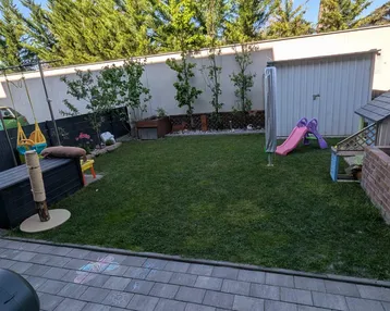 Gepflegter Gartenbereich mit Rasenfläche, Spielgeräten und einem Gartenhaus.