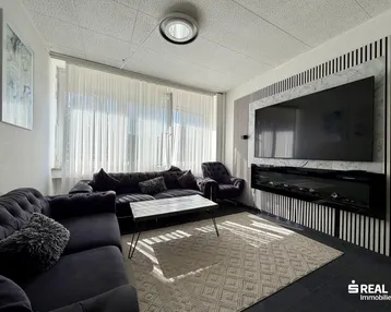 Gemütliches Wohnzimmer mit großer Couch, modernem TV-Bereich und viel Tageslicht durch große Fenster.