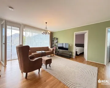 Helles Wohnzimmer mit Parkettboden, gemütlicher Sitzecke und Zugang zum Balkon.