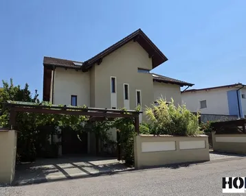 Modernes Einfamilienhaus mit Satteldach, Carport und gepflegter Vorgartengestaltung unter blauem Himmel.