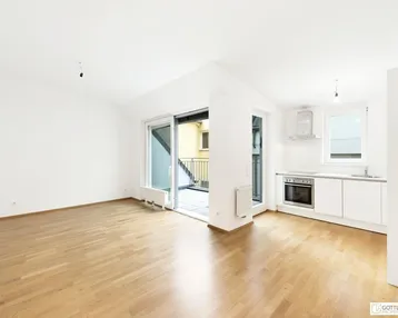 Heller Wohnbereich mit Parkettboden, integrierter Küchenzeile und Zugang zum Balkon.