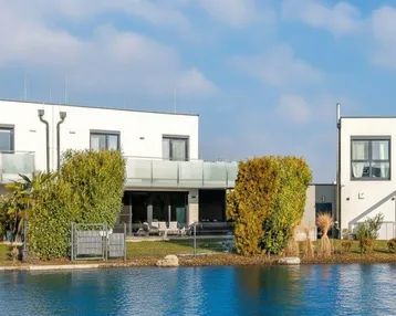Moderne weiße Gebäude am Wasser mit gepflegter Gartenanlage und klarem Himmel.