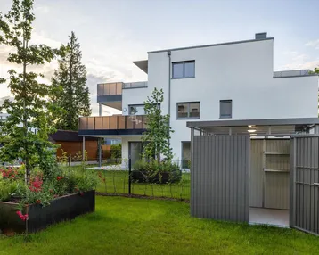Modernes weißes Mehrfamilienhaus mit Balkonen, gepflegtem Rasen und einem Hochbeet im Vorgarten.