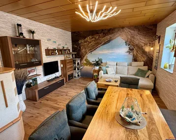Gemütlicher Wohn-Essbereich mit Holzboden, großem Esstisch und einer modernen Couch.