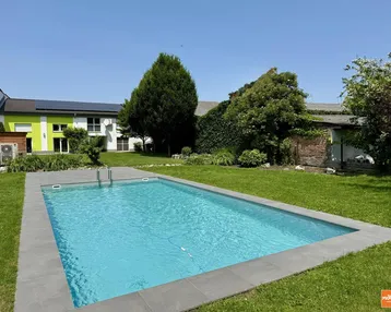 Großer Außenpool im gepflegten Garten mit Rasenfläche und sonniger Umgebung.