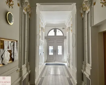 Elegante Eingangshalle mit Stuckverzierungen, hohen Decken und klassischem Fliesenboden in einem Altbau.