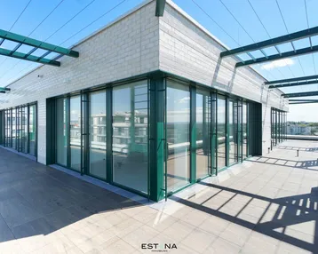 Große Dachterrasse eines modernen Gebäudes mit raumhohen Fenstern und grünen Akzenten.