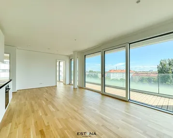 Heller, moderner Wohnbereich mit Parkettboden, großen Fenstern und Zugang zum Balkon.