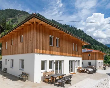 Modernes Haus mit Holzfassade und weißem Putz, umgeben von Bergen, mit gemütlicher Terrasse.