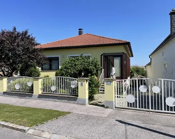 Gelbes Einfamilienhaus mit rotem Ziegeldach, Vorgarten und weißem Gartentor.