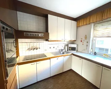 Küche mit weißen Einbauschränken, Holztheke, integrierten Geräten und Fliesenrückwand.
