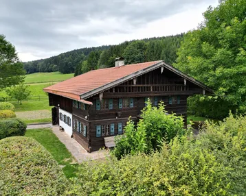 Traditionelles Holzhaus mit rotem Ziegeldach, grüner Umgebung und weitem Blick auf die Landschaft.