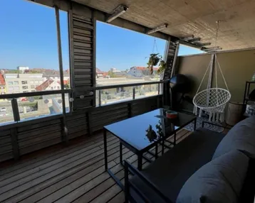 Geräumiger Balkon mit Holzfußboden, bequemen Möbeln und weitem Blick über die Stadt.