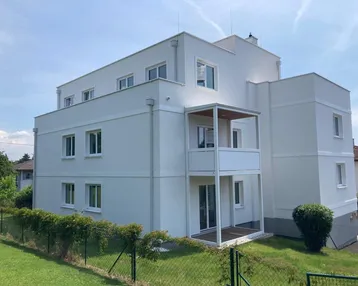 Modernes Mehrfamilienhaus mit weißer Fassade und Balkonen in grüner Umgebung.