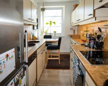 Funktionale Küche mit Holz-Arbeitsplatten, integrierten Geräten und einem Fenster für natürliches Licht.