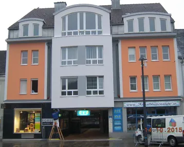 Fassade eines Mehrzweckgebäudes mit orangefarbenen Akzenten und modernen Fenstern im Zentrum.