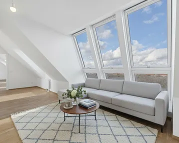 Helles Wohnzimmer in einer Dachgeschosswohnung mit großen Dachfenstern, modernem Sofa und Holzboden.