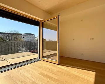 Helles Zimmer mit Holzboden und Zugang zu einem Balkon, ideal für Wohn- oder Schlafbereich.