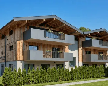 Modernes Gebäude mit Holzfassade, grauen Balkonen und gepflegter Hecke.