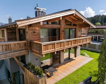 Modernes Holzchalet mit großem Balkon und Sonnenterrasse, umgeben von Grün.