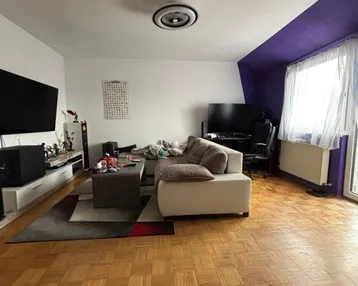 Gemütliches Wohnzimmer mit Parkettboden, beiger Couch und einer auffälligen lila Akzentwand.