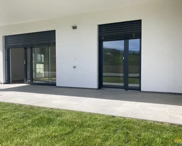 Große, geflieste Terrasse mit direktem Zugang zu den Innenräumen und angrenzender Rasenfläche.