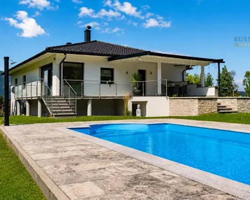 Modernes Haus mit großem Pool, weitläufigem Garten und Bergblick unter blauem Himmel.