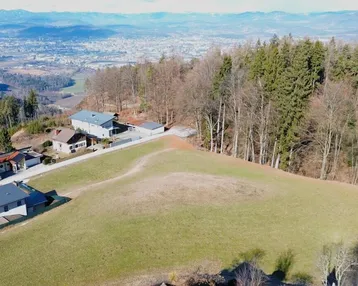 Luftaufnahme eines weitläufigen Grundstücks mit mehreren Häusern, Wald und Bergblick in der Ferne.