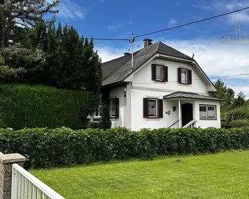 Charmantes Einfamilienhaus mit Satteldach, umgeben von gepflegtem Rasen und hohen Hecken.